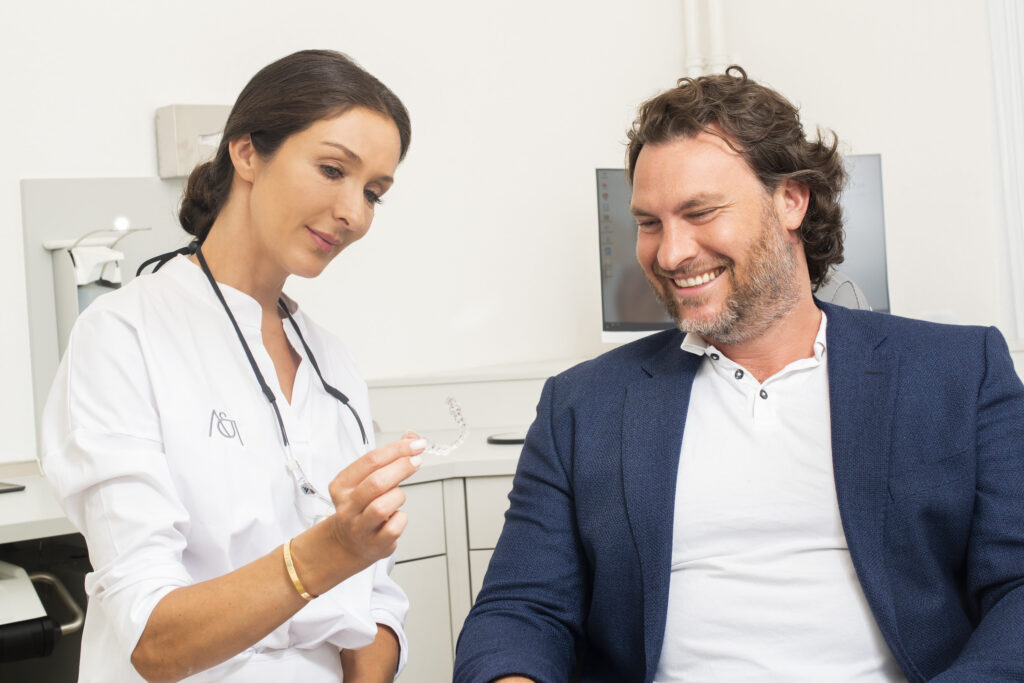 Dr. Indin zeigt einem Patienten eine transparente Aligner-Schiene in der Praxis in Offenbach