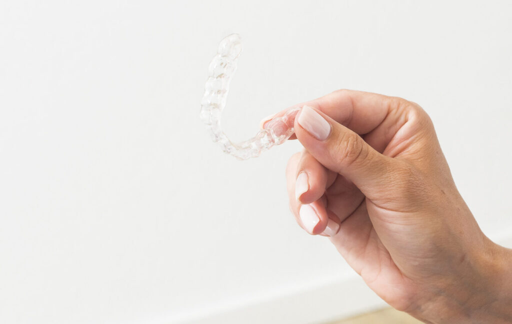 Hand hält eine transparente Aligner-Schiene zur unauffälligen Zahnkorrektur bei Erwachsenen