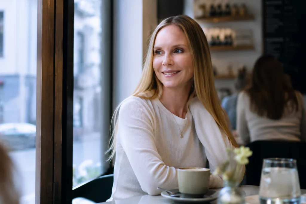 Frau mit Kaffeetasse im Café, Kaffee und Rotwein begünstigen Verfärbungen an Veneers