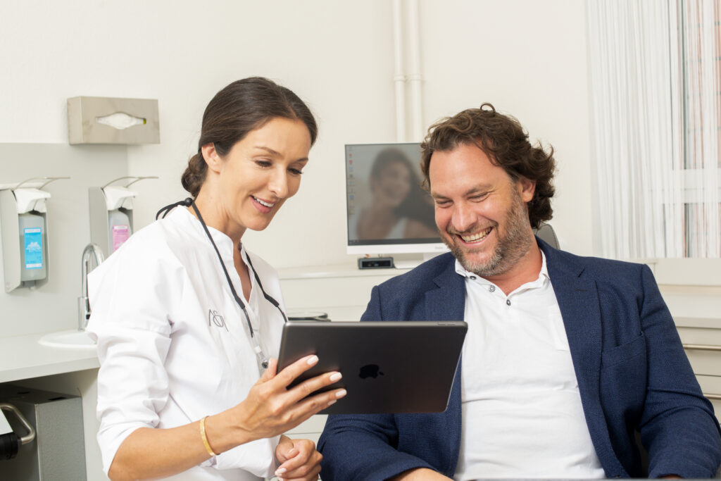 Dr. Indin zeigt einem Patienten Befunde auf dem Tablet in der Zahnarztpraxis Offenbach – Parodontitis-Behandlung